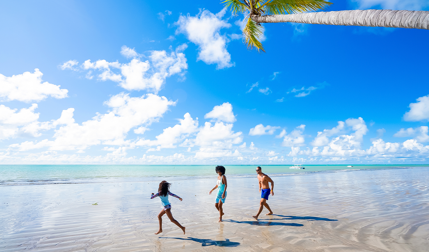 Família aproveitando o mar calmo e paradisíaco na Praia de Ipioca, com água rasa e azusi, céu azul e horizonte aberto.