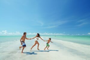 Família correndo de mãos dadas pela praia.