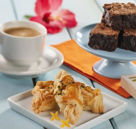 Mesa com café, brownies de chocolate e croissant em ambiente aconchegante, ideal para café da manhã ou lanche da tarde.