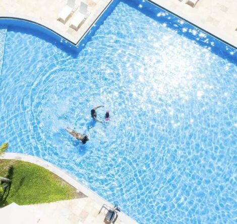 Piscina azul cintilante em resort com piscina aquecida, vista de cima, com hóspedes nadando e relaxando sob o sol.