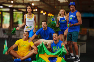 Grupo de quinto amigos torcedores usando camisas do Brasil, segurando bandeiras e vuvuzela em clima de jogo no Salinas Maceió.