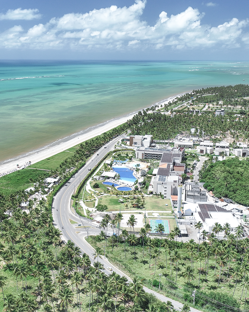 Vista aérea do Japaratinga Lounge Resort, com suas acomodações, diversos pontos de consumo e complexo de piscinas, rodeado por uma densa vegetação nativa e à beira mar.
