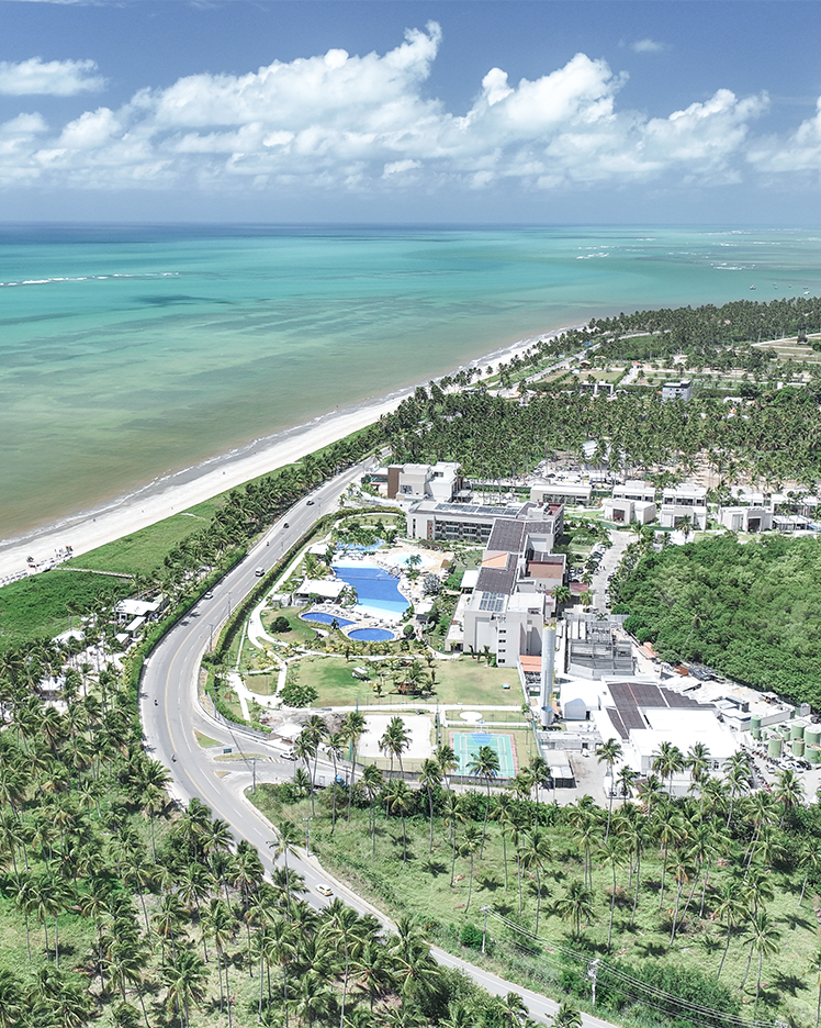 Vista aérea do Japaratinga Lounge Resort, com suas acomodações, diversos pontos de consumo e complexo de piscinas, rodeado por uma densa vegetação nativa e à beira mar.