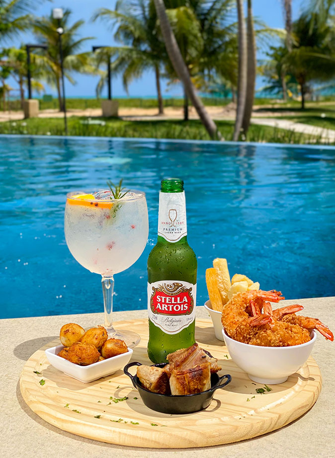 A foto representa um pouco do all inclusive do Salinas Maragogi, um dos melhores resorts do Nordeste. Há petiscos de camarão, caipirinha, cerveja long neck e outras porções de petiscos.