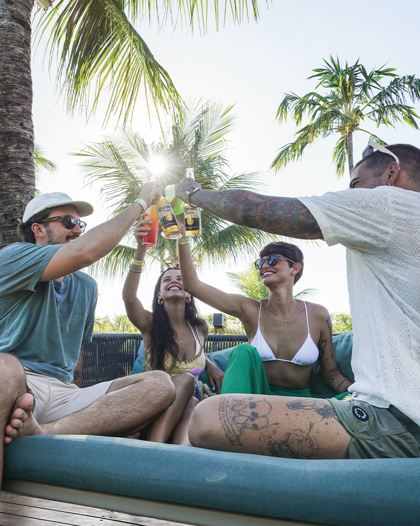 drinks com amigos Quatro amigos sentados no banco próximo à Vila da Praia. São dois homens e suas mulheres, os homens estão com long neck de Corona na mão e as mulheres com drinks coloridos, é fim de tarde com o fundo de coqueiros.