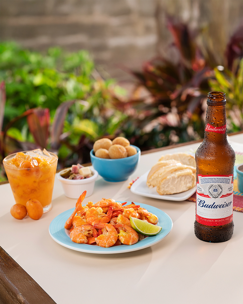 resort all inclusive Cerveja long neck Budweiser ao lado camarões, drink de cajá, paes e coxinhas, disponíveis no resort All Inclusive Salinas Maceió sobre mesa branca.